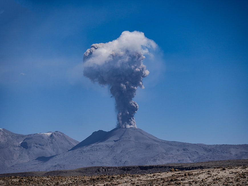 Active Volcanic Eruption With Ash Cloud Rising Over Mountainous Landscape