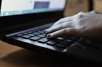 Close-up of hand typing on black laptop keyboard