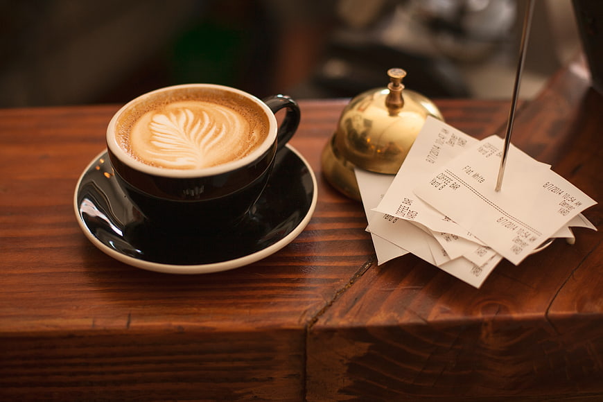 Latte Art Coffee Cup with Service Bell and Receipts on Wooden Counter