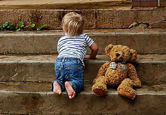 Toddler crawling up concrete steps with teddy bear