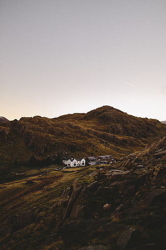 Lone white building nestled in rugged mountain landscape at dusk
