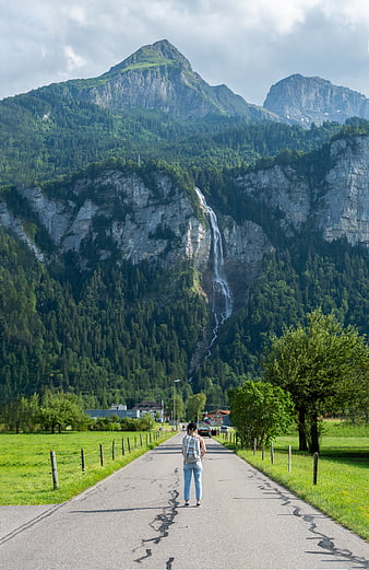 Woman walking on road towards mountain waterfall landscape