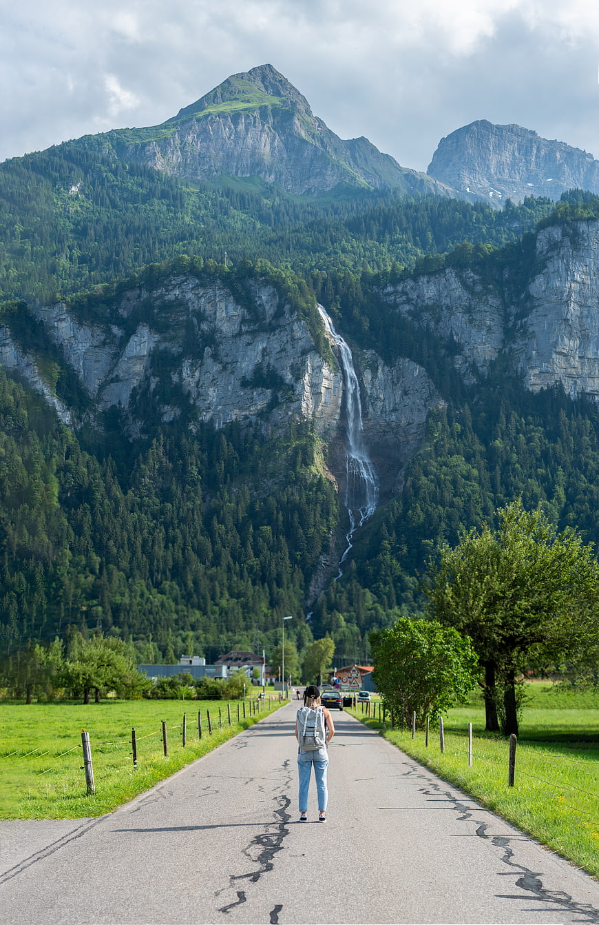 Woman walking on road towards mountain waterfall landscape