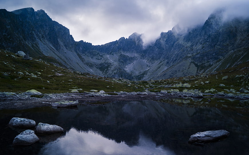Dramatic mountain landscape with lake reflection and misty peaks