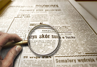 Hand holding magnifying glass over vintage Polish newspaper text