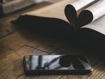 Black smartphone on rustic wooden desk with open book and heart bookmark