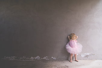 Lonely toddler girl in pink tutu against gray wall