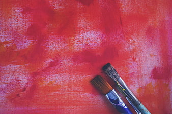 Two paint brushes on a textured red and pink abstract background