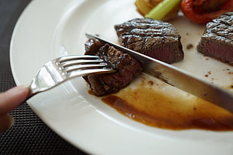 Close-up of knife and fork cutting into a juicy medium-rare steak