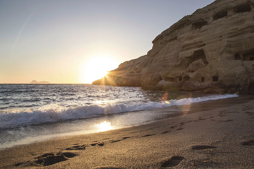 Sunset on sandy beach with footprints and ancient cliffside ruins