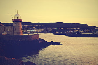 Lighthouse at Harbor Dusk with Coastal Town Background