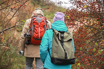 Two Hikers Walking Through Autumn Forest With Backpacks