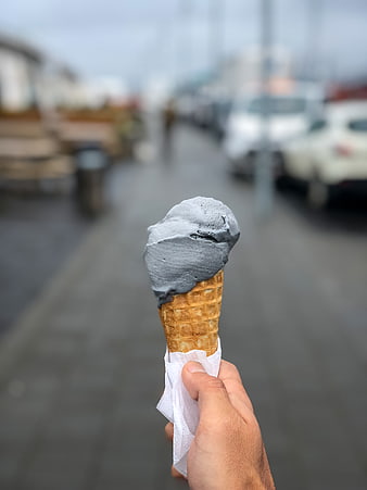 Hand holding grey ice cream cone on blurred street
