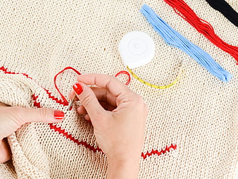 Hands Embroidering Red Pattern on Beige Knitted Sweater