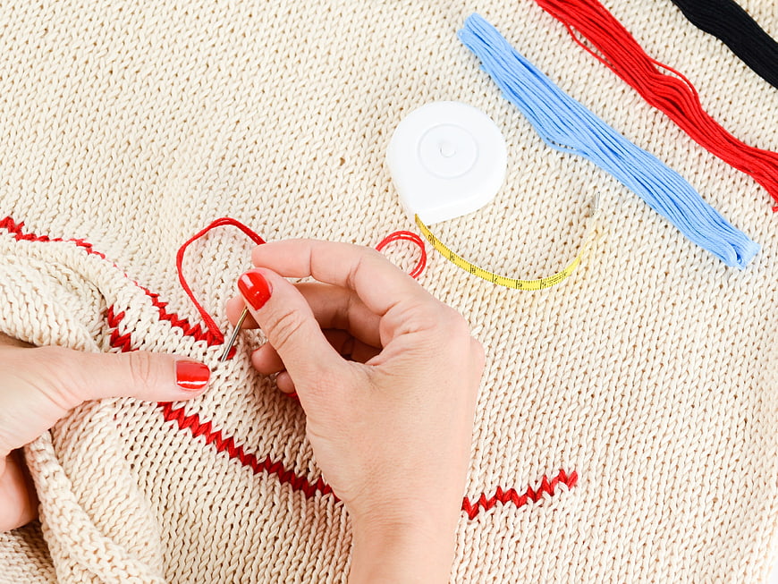 Hands Embroidering Red Pattern on Beige Knitted Sweater
