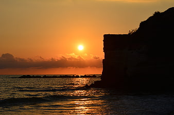 Silhouette of coastal cliff against golden sunset over ocean