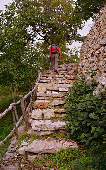 Hiker with backpack ascending ancient stone steps in Italian forest