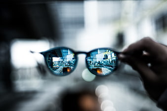 Hand holding sunglasses reflecting city bridge and buildings