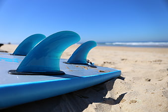 Close-up of blue surfboard fins on a sunny sandy beach