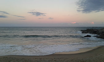 Serene Beach Sunset with Gentle Waves and Rocky Shoreline