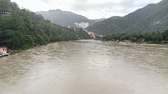 Wide muddy Ganges river flowing through lush green mountain valley