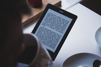 Person reading Kindle e-reader with coffee cup
