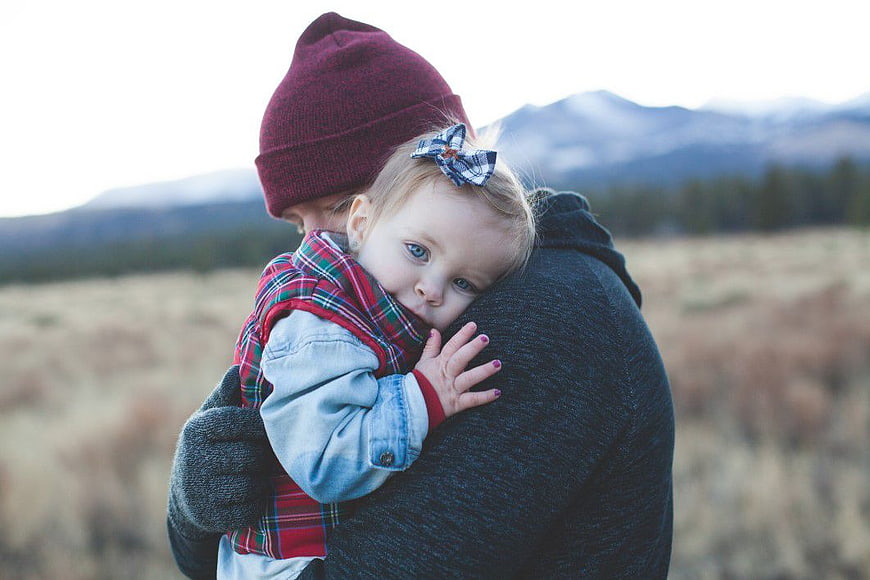 Father holding baby girl in plaid vest outdoors