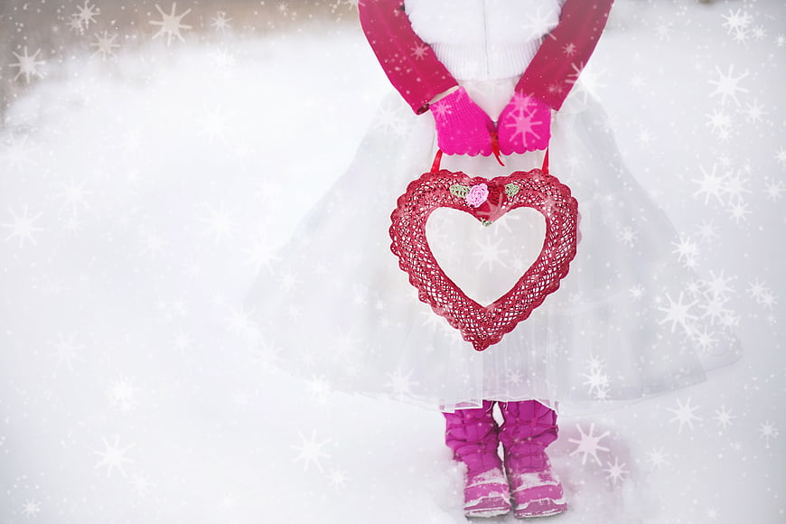 Child in white tutu holding red heart basket in snow