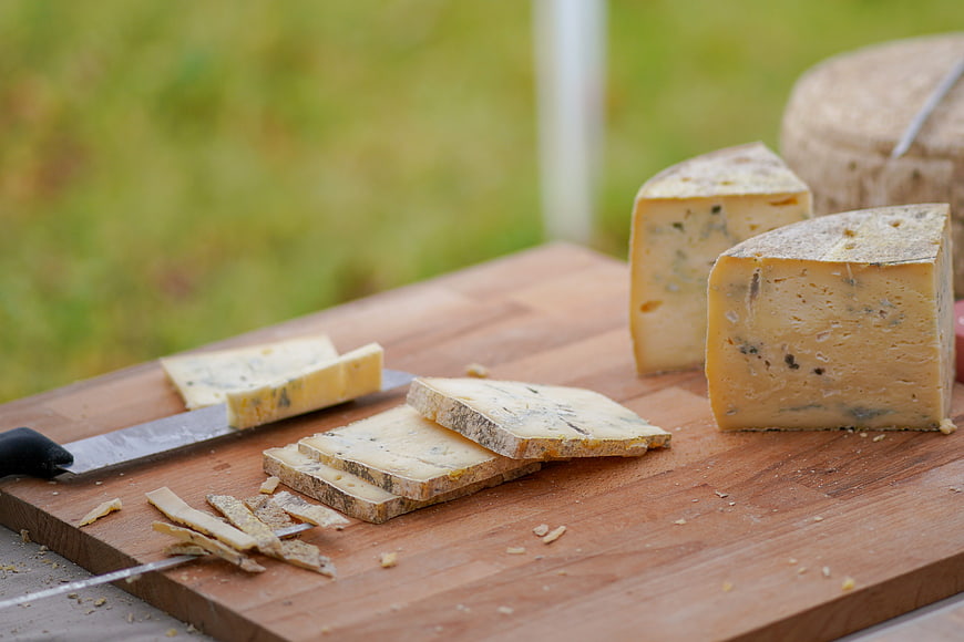 Sliced hard cheese on wooden cutting board with knife
