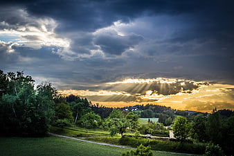 Dramatic Sun Rays Breaking Through Storm Clouds Over Green Landscape