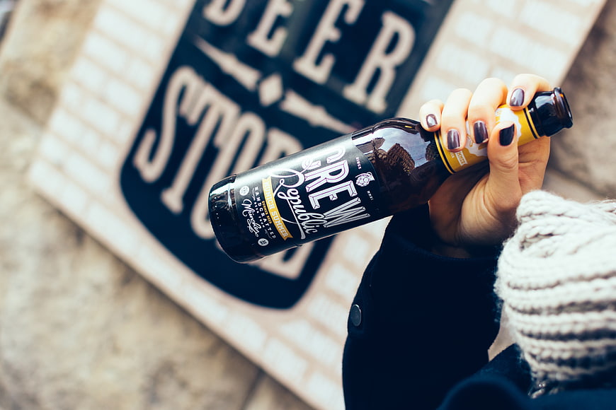 Woman holding beer bottle in front of brewery sign