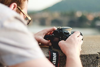 Man holding DSLR camera with blurred landscape background