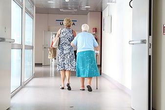 Senior woman assisting elderly friend with cane in hospital corridor
