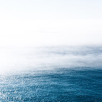 Aerial view of blue ocean waves fading into white fog