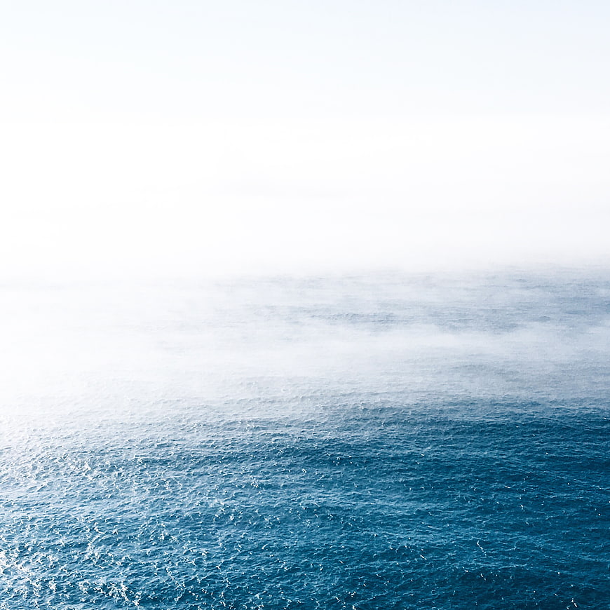 Aerial view of blue ocean waves fading into white fog