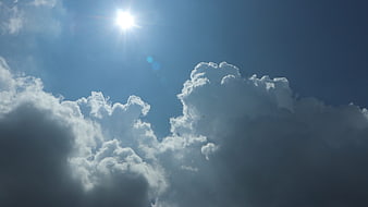 Bright Sun Shining Through Fluffy White Clouds in Blue Sky