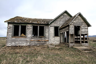 Abandoned weathered wooden farmhouse in rural field