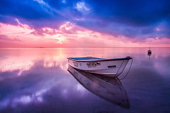 Lone boat on wet sand reflecting vibrant pink and blue sunset sky