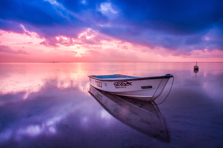 Lone boat on wet sand reflecting vibrant pink and blue sunset sky