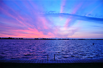 Vibrant purple and pink sunset over a lake with wooden dock