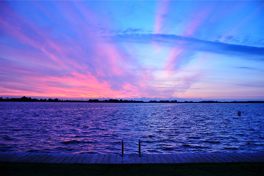 Vibrant purple and pink sunset over a lake with wooden dock