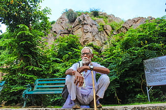 Senior Indian man with walking stick sitting in park