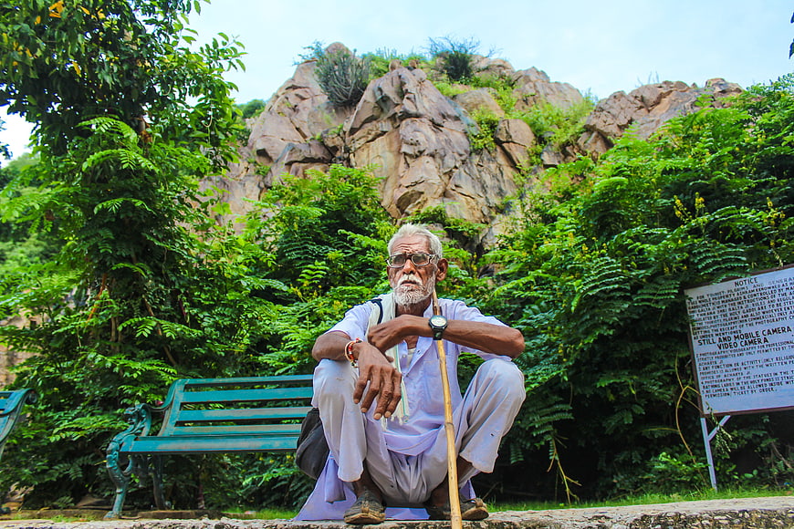 Senior Indian man with walking stick sitting in park