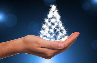 Glowing star Christmas tree held in open hand on dark blue background