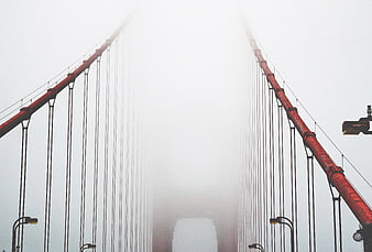 Red suspension bridge disappearing into thick white fog