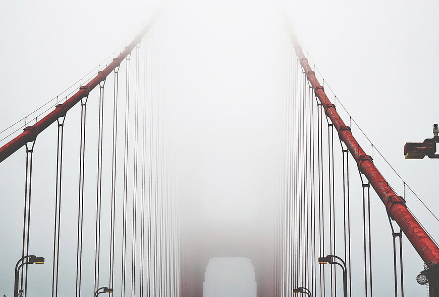 Red suspension bridge disappearing into thick white fog