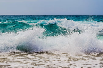 Powerful turquoise ocean wave crashing on sandy beach