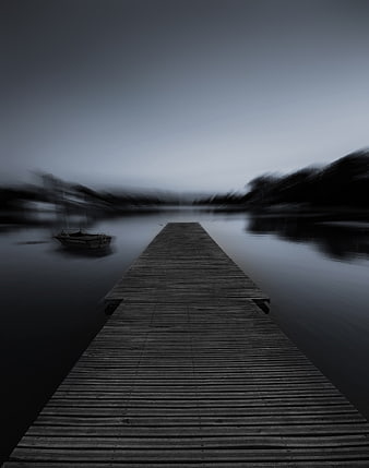 Moody wooden pier extending into misty lake with blurred boat
