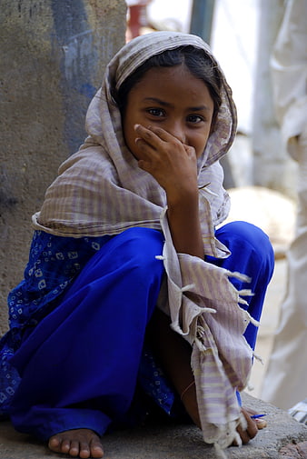 Shy young girl in traditional blue clothing sitting outdoors