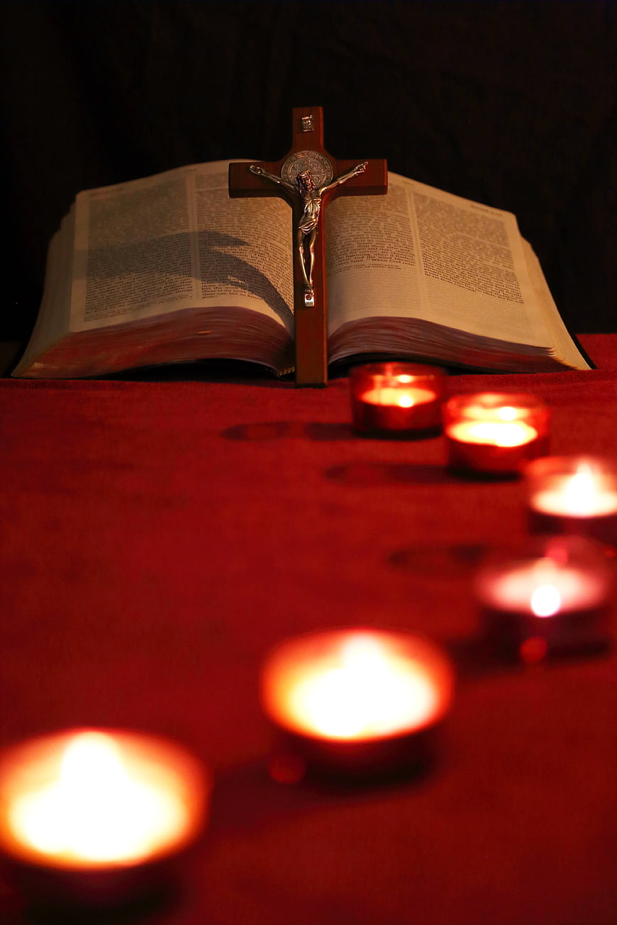 Crucifix on open Bible with red votive candles